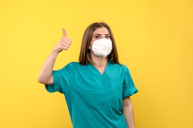 Vue de face de femme médecin avec masque sur mur jaune