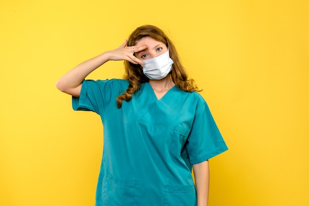 Vue de face de la femme médecin en masque sur mur jaune