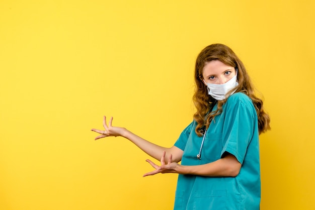 Vue de face de la femme médecin en masque sur mur jaune