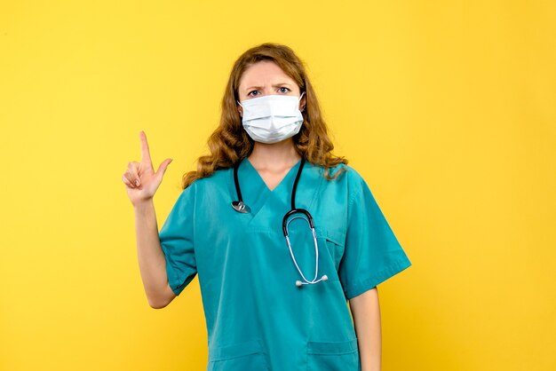 Vue de face de la femme médecin en masque sur mur jaune