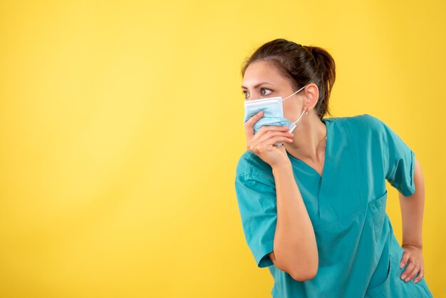 Vue de face femme médecin en masque de protection sur fond jaune