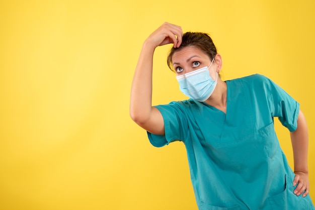 Vue de face femme médecin en masque de protection sur fond jaune