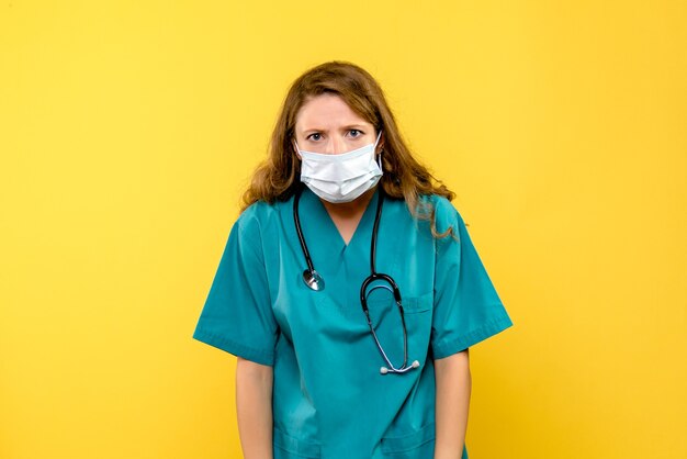 Vue de face de la femme médecin en masque stérile sur mur jaune