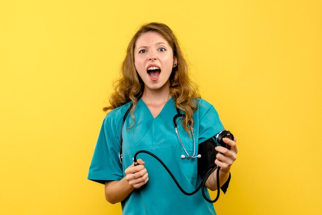 Vue de face de la femme médecin mesurant la pression sur le mur jaune