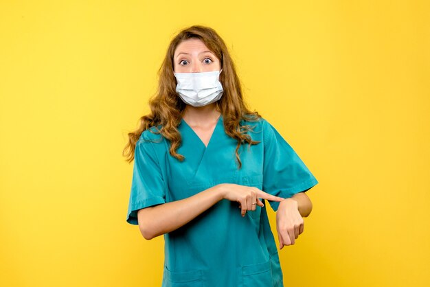 Vue de face de femme médecin pointant sur le poignet sur le mur jaune