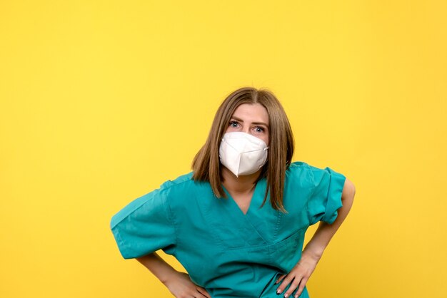 Vue de face femme médecin posant avec masque sur espace jaune