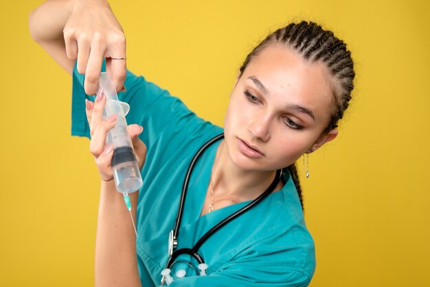 Vue de face de la femme médecin prépare une énorme injection sur mur jaune