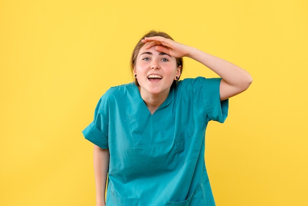 Vue de face femme médecin à la recherche à distance sur fond jaune santé émotion hospital medic