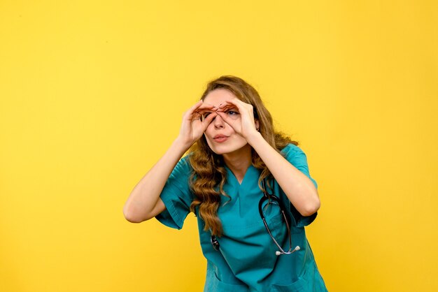 Vue de face de la femme médecin regardant à travers les doigts sur le mur jaune