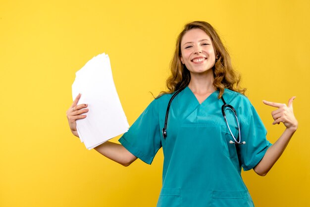 Vue de face de la femme médecin souriant avec des fichiers sur le mur jaune