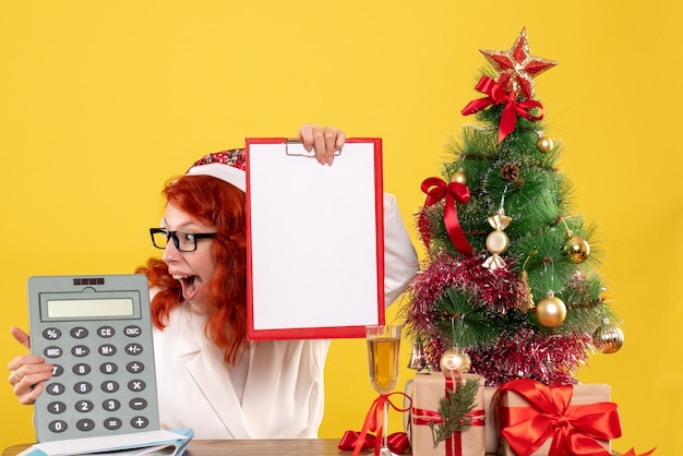 Vue de face femme médecin tenant calculatrice autour des cadeaux de Noël et arbre