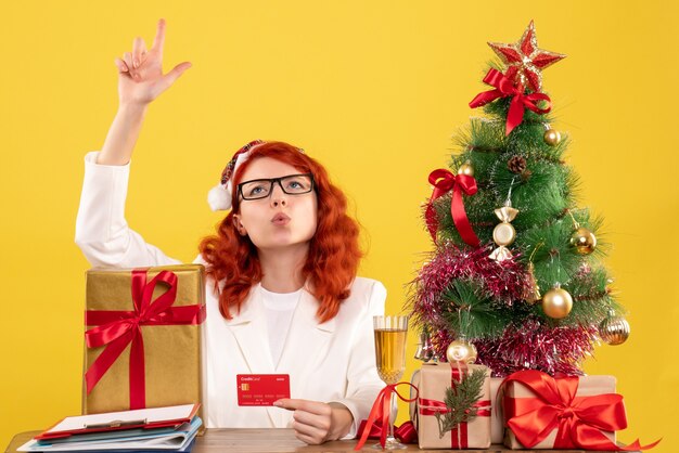 Vue de face femme médecin tenant une carte bancaire autour de cadeaux de Noël et arbre