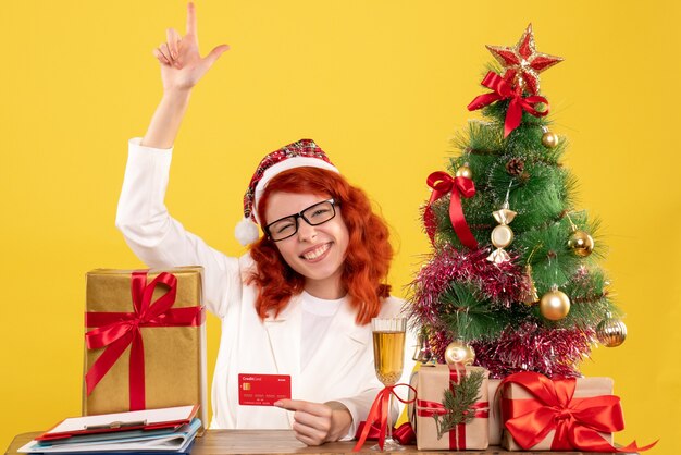 Vue de face femme médecin tenant une carte bancaire autour de cadeaux de Noël et arbre