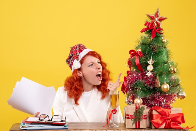 Vue de face femme médecin tenant des documents et assis avec des cadeaux de Noël