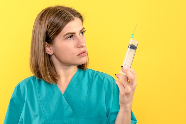 Vue de face femme médecin tenant grosse injection sur espace jaune