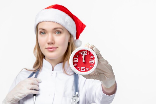 Vue de face d'une femme médecin tenant une horloge sur un mur blanc