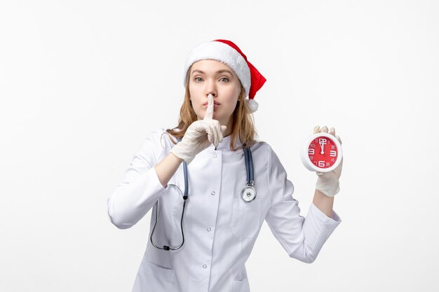 Vue de face d'une femme médecin tenant une horloge sur un mur blanc