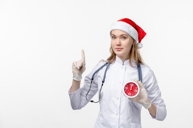 Vue de face d'une femme médecin tenant une horloge sur un mur blanc