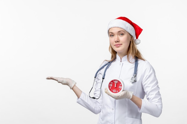 Vue de face d'une femme médecin tenant une horloge sur un mur blanc