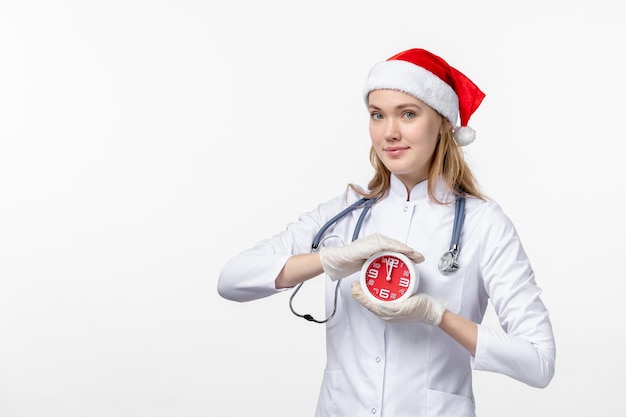 Vue de face d'une femme médecin tenant une horloge sur un mur blanc