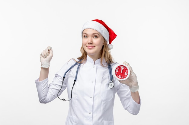 Vue de face d'une femme médecin tenant une horloge sur un mur blanc