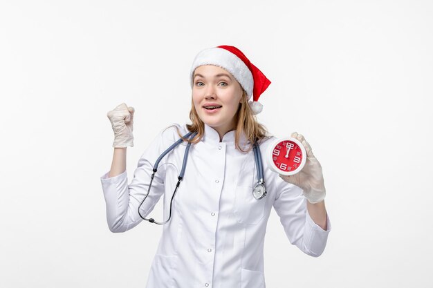 Vue de face d'une femme médecin tenant une horloge sur un mur blanc