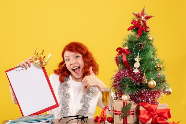 Vue de face femme médecin tenant note de fichier autour de l'arbre de Noël et présente