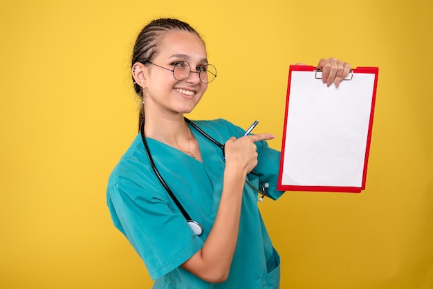 Vue de face femme médecin tenant presse-papiers médical et stylo avec sourire, couleur infirmière hôpital émotion covid-19 medic health