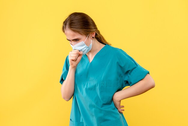 Vue de face femme médecin toux sur fond jaune pandémie de l'hôpital de covid- santé