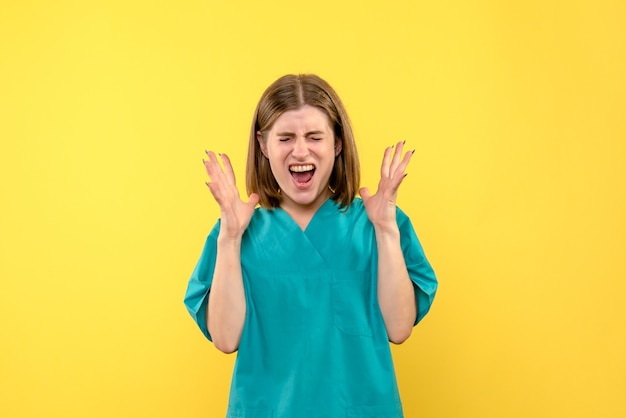 Vue de face de femme médecin avec visage hurlant sur mur jaune