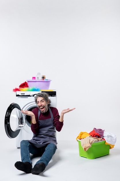 Vue de face femme de ménage ravie assise devant la laveuse ouvrant les mains panier à linge sur fond blanc