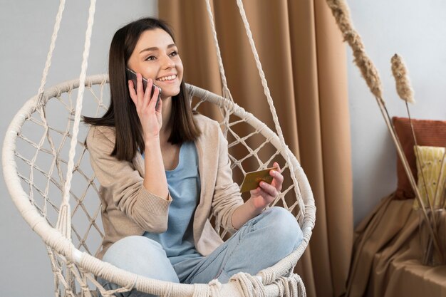 Vue de face de femme parlant sur smartphone et tenant une carte de crédit