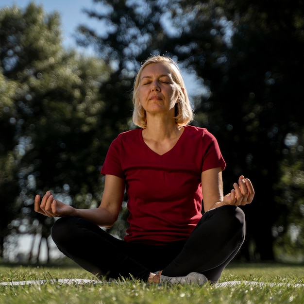 Vue de face d'une femme plus âgée en position du lotus à l'extérieur pendant le yoga