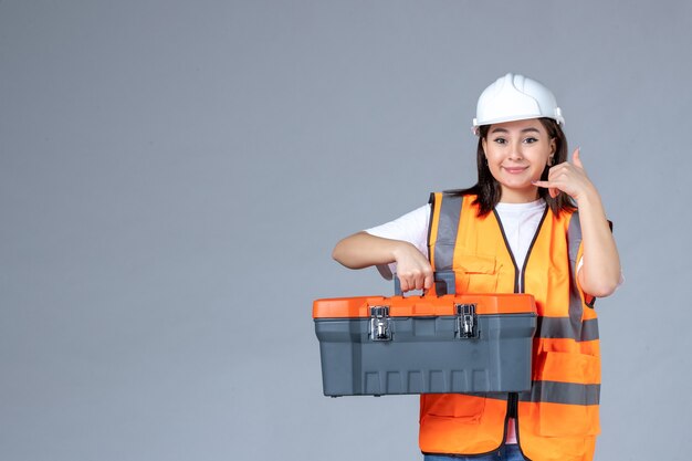 Vue de face d'une femme portant une mallette à outils lourde sur un mur blanc