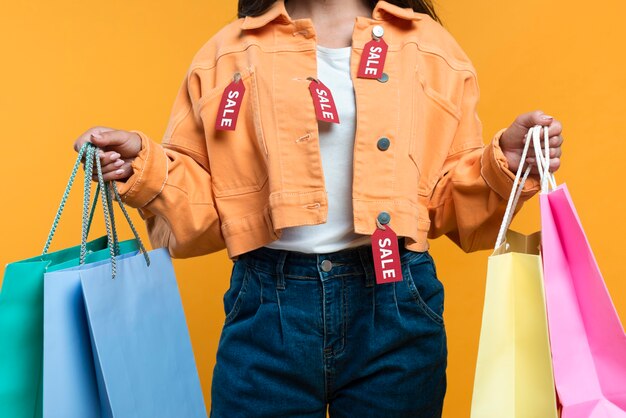 Vue de face de la femme portant une veste avec des étiquettes et tenant des sacs à provisions