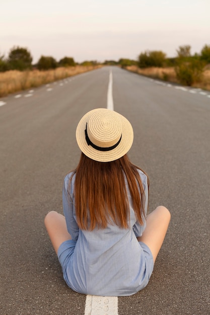 Vue de face de la femme posant au milieu de la route avec un chapeau