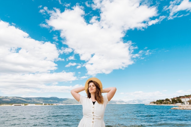 Photo gratuite vue de face de femme posant à l'océan avec des nuages dans le ciel