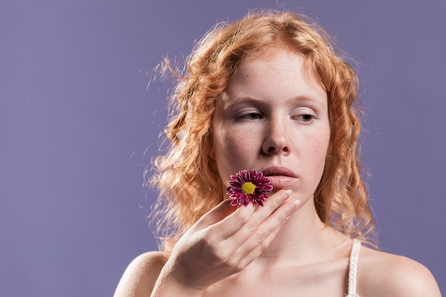 Vue de face de femme rousse tenant une fleur près de sa bouche avec copie espace