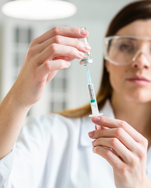 Vue de face de la femme scientifique avec des lunettes de sécurité tenant une seringue avec un vaccin