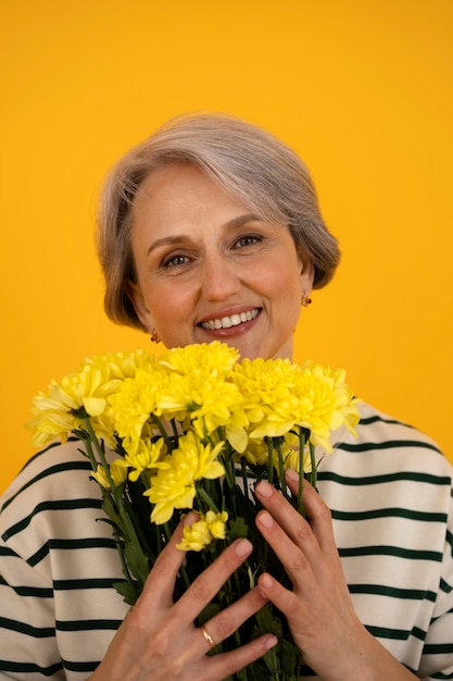 Vue de face femme senior posant avec des fleurs