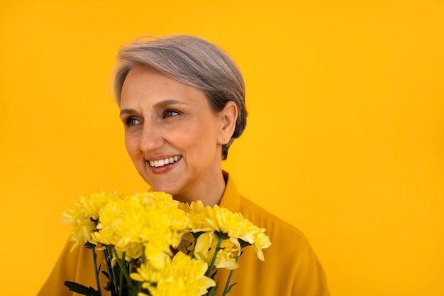 Vue de face femme senior posant avec des fleurs