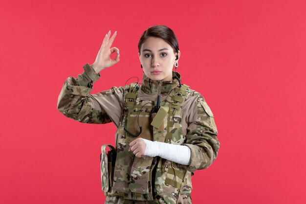 Vue de face femme soldat en camouflage avec mur rouge bras cassé