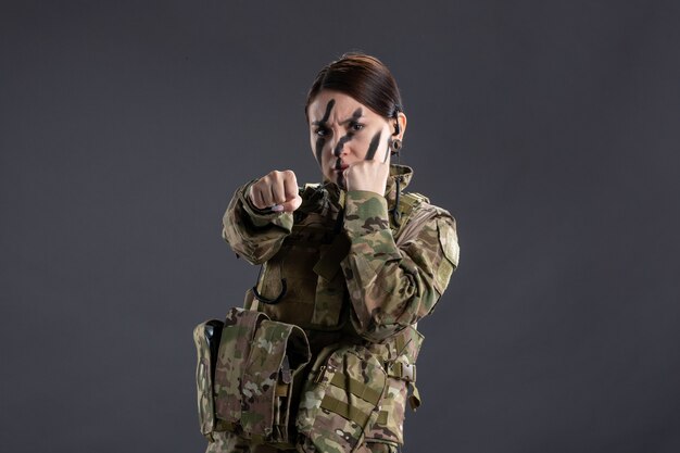 Vue de face d'une femme soldat en camouflage sur le mur sombre