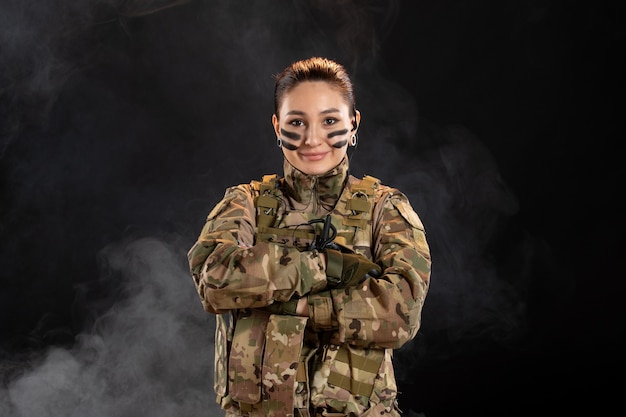 Vue de face d'une femme soldat en camouflage sur le mur sombre