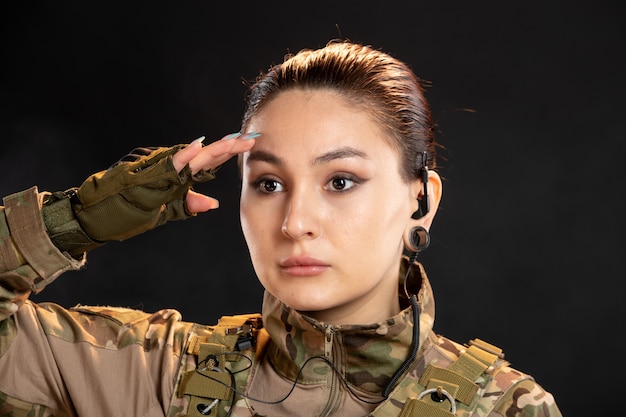 Photo gratuite vue de face d'une femme soldat en camouflage saluant sur un mur noir