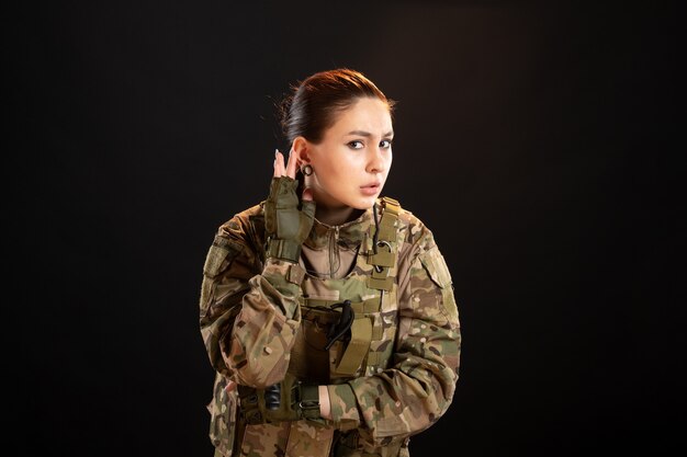 Vue de face d'une femme soldat écoutant sur un mur noir