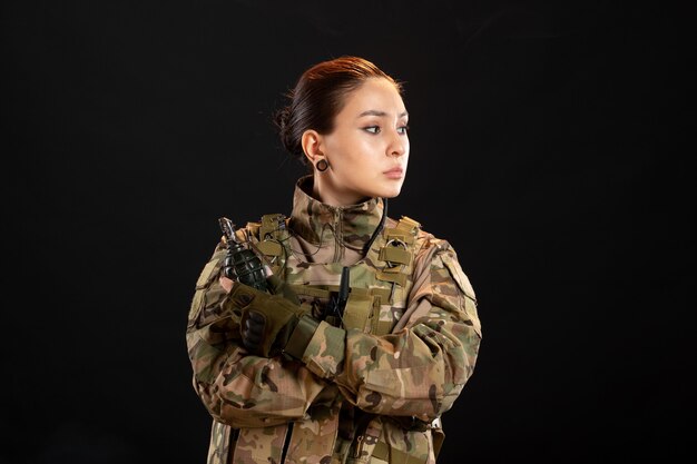 Vue de face d'une femme soldat avec grenade en uniforme sur mur noir