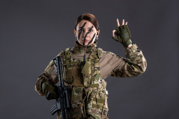 Vue de face femme soldat avec mitrailleuse en camouflage sur mur sombre