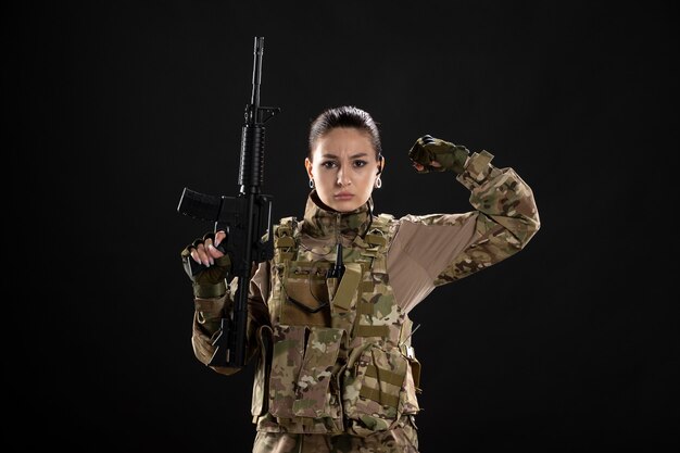 Vue de face femme soldat en uniforme avec fusil sur mur noir