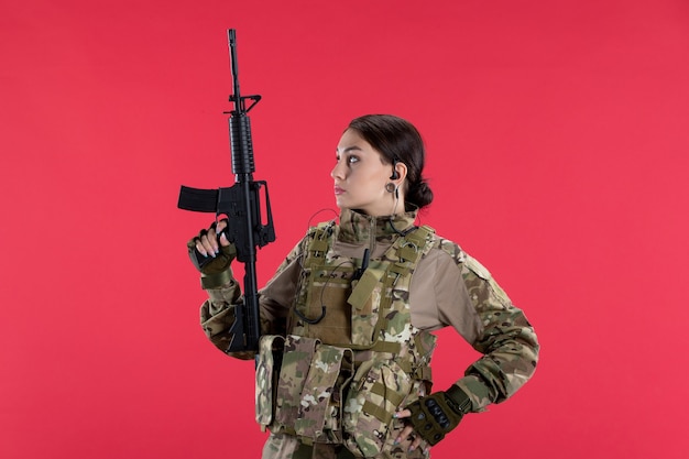 Photo gratuite vue de face femme soldat en uniforme militaire avec mur rouge de mitrailleuse